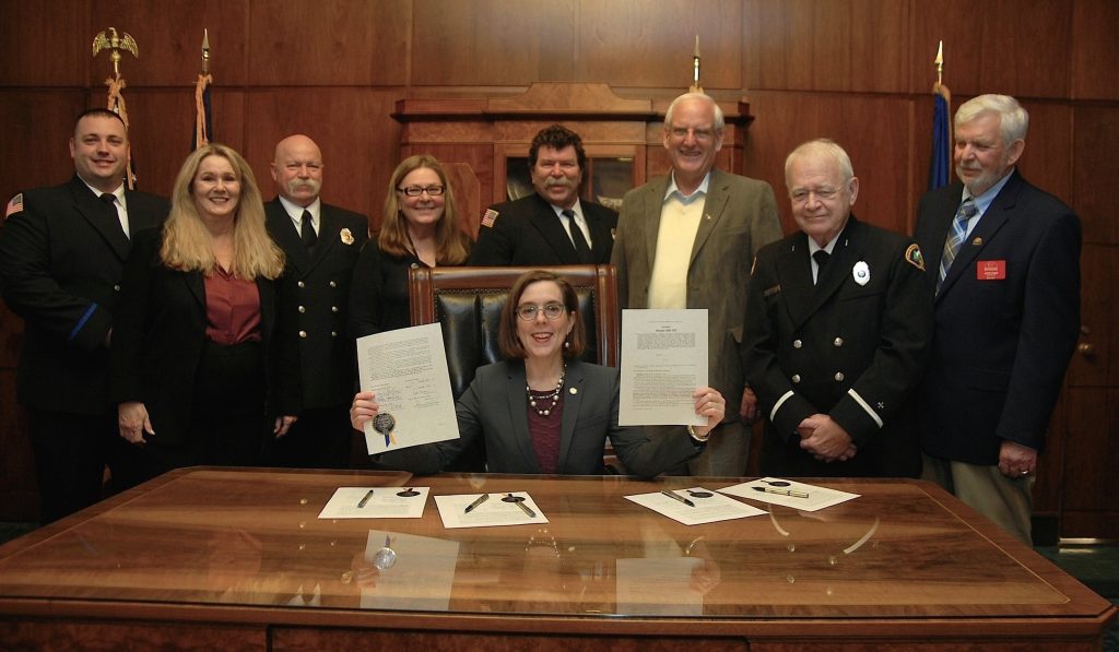 Gov. Kate Brown holds up signed legislation for SB378, which supports Oregon's fire service emergency responders such as firefighters and EMTs. 